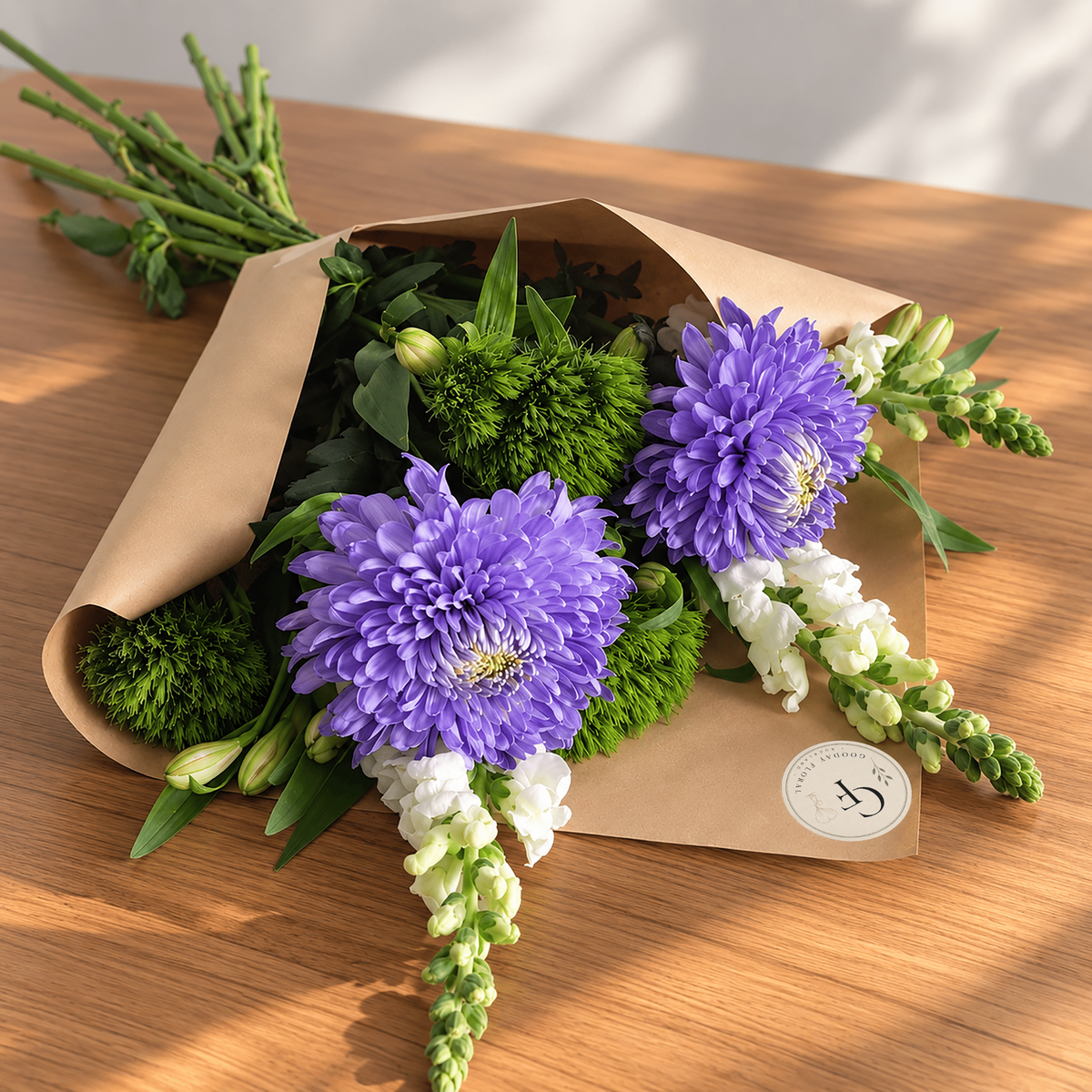 Classic bouquet with purple chrysanthemums, white snapdragons and green foliage in kraft wrapping.