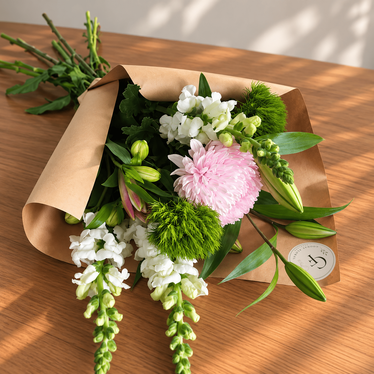 Petite bouquet with a pink chrysanthemum, white snapdragons and green foliage in kraft wrapping.