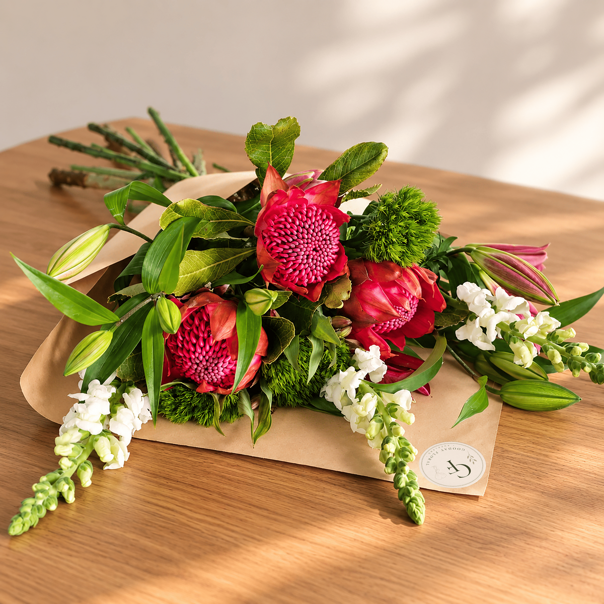 Statement bouquet with red waratahs, white snapdragons, lily buds and green foliage in kraft wrapping.